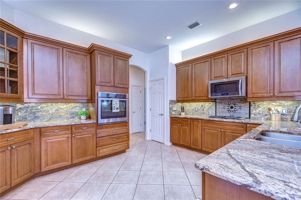 Beautiful kitchen features 42” wood cabinets topped with crown and uplighting, stainless appliances including a built-in oven and gas burner cooktop, beautiful granite countertops, and granite backsplash!