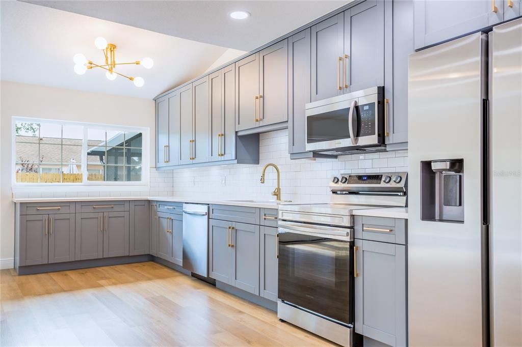 The spacious designer kitchen with brand new Samsung appliances and quartz countertops provide a sleek contrast to the clean subway tile backsplash, creating a space that's both functional and visually appealing.
