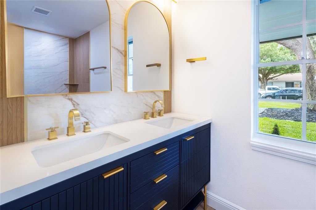 Primary ensuite is a luxurious retreat with marble and wood ceramic tile, complemented by a modern gold shower faucet set featuring a shower head and handheld. The navy blue Vanity adds a touch of sophistication.