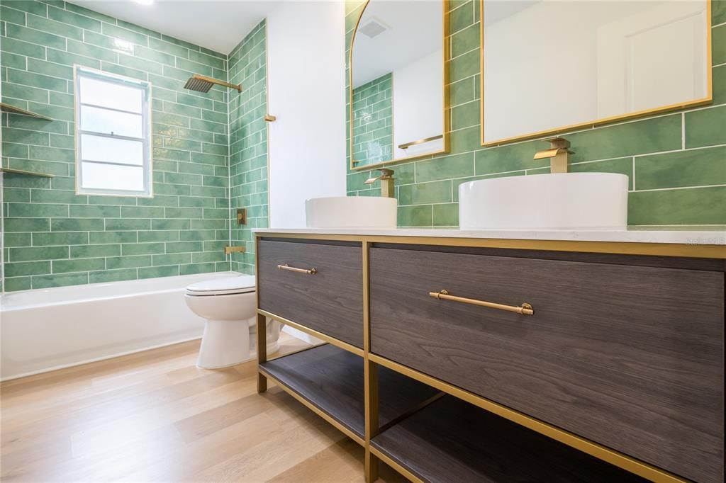 Secondary bathroom has modern green subway tiles paired with a luxury wood Vanity, a spacious bathtub, and a gold Shower Faucet Set, offering both functionality and elegance.