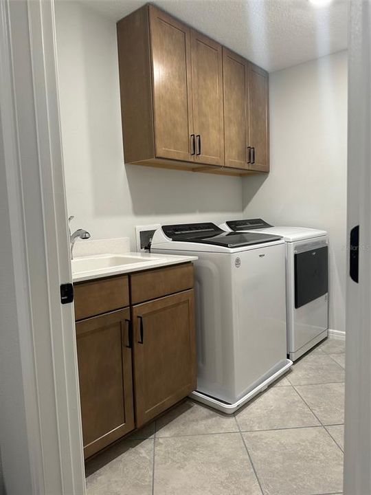 upgraded laundry room with cabinets, sink, and quartz countertops