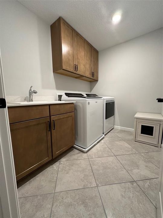 upgraded laundry room with cabinets, sink, and quartz countertops