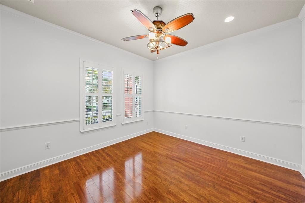 Large classic first floor study or office with french doors,  hardwood floors, plantation shutters, and nautical light/fan ceiling fixture.