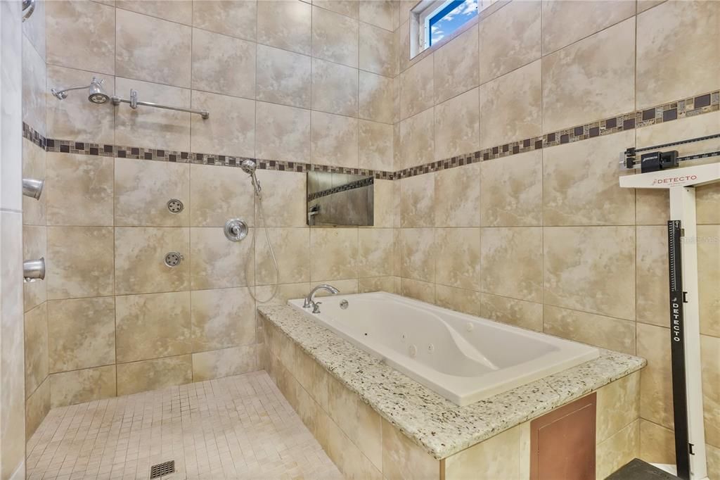 Spa inspired master bath featuring a jetted hydro tub, a spacious shower stall with dual shower heads, floor to ceiling tile and a separate toilet stall.