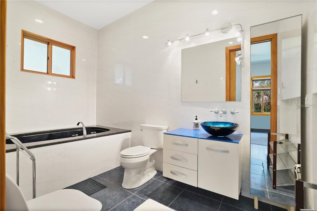 2nd bath with jetted hydro tub, shower and custom vanity with a glass bowl sink.