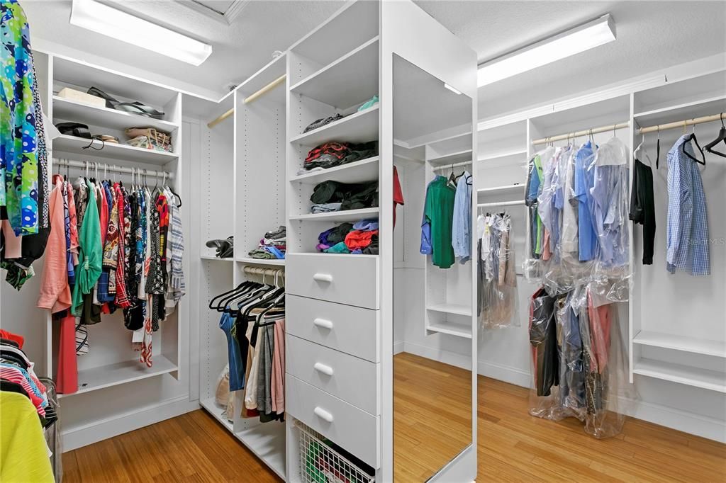 The expanded his/her walk-in closet with closet organizers within the primary bedroom