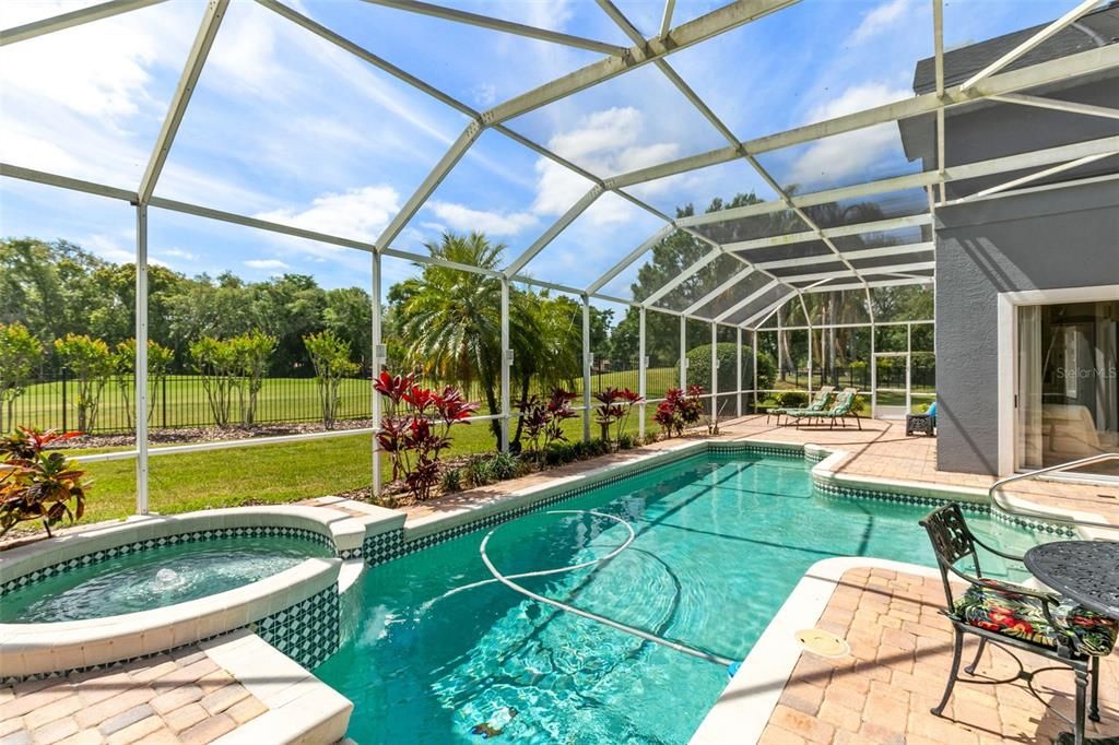 Screened pool and spa overlooks the lush fenced lawn and golf course.