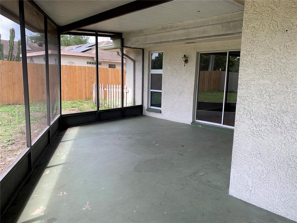 Large outdoor screened in patio/lanai across back of home with fenced yard.