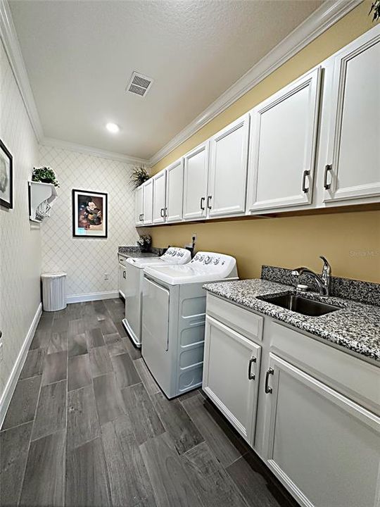 Upstairs laundry with built in upper and lower cabinets, granite counters, sink and built in ironing board