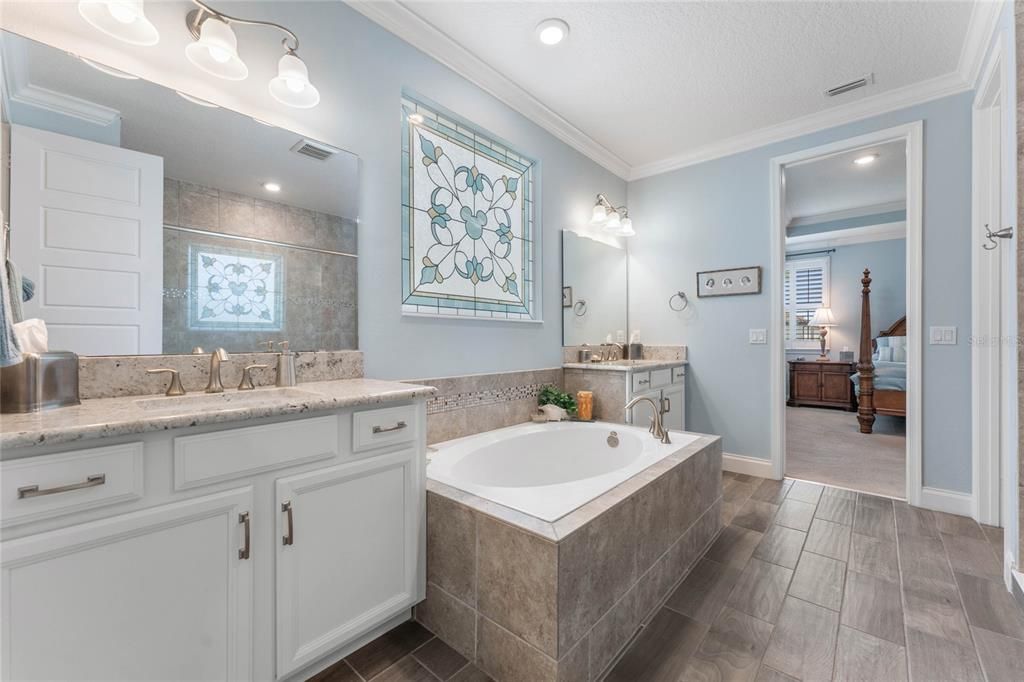Primary bath with large soaking tub, separate vanities with granite counters, Huge walk in shower with frameless glass, crown molding and custom stained glass insert.