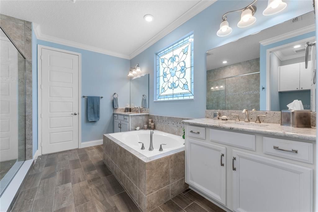 Primary bath with large soaking tub, separate vanities with granite counters, Huge walk in shower with frameless glass, crown molding and custom stained glass insert. Huge walk in closet behind 8' door