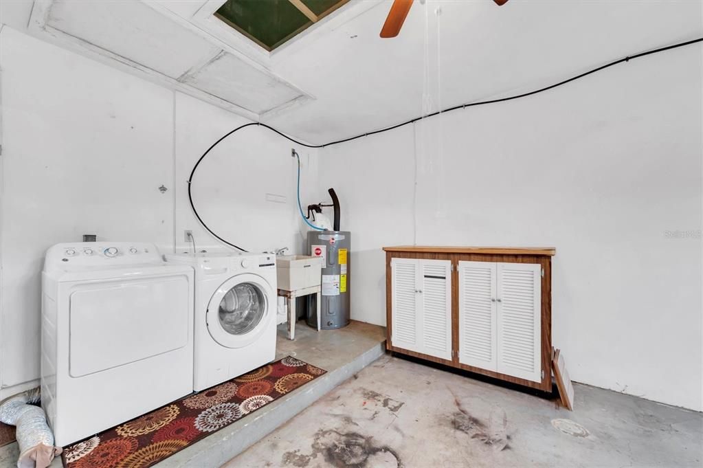 Washer, dryer, cleaning sink and full size water heater at back end of garage