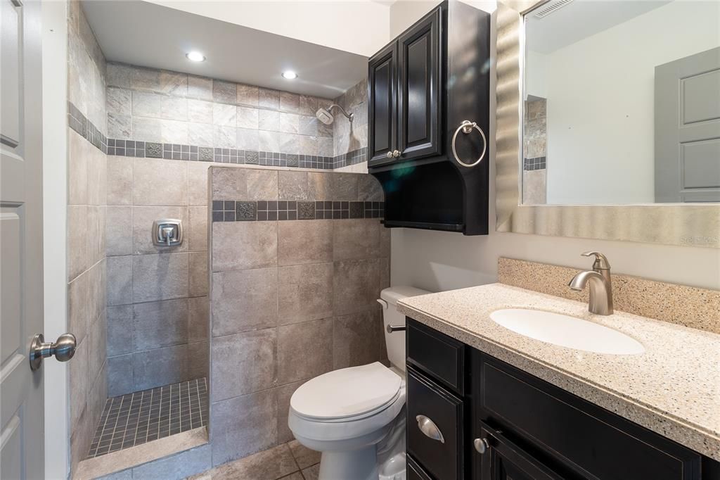 Primary bathroom European walk-in shower with wall to floor tile, Corian counter top and custom antiqued cabinets.