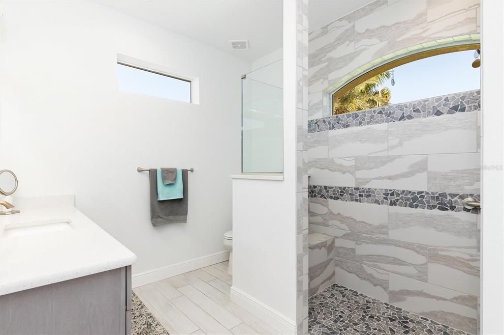 Carrying over the same neutral earth tones and materials, the second primary bath includes a spacious shower with bench for safety and convenience.