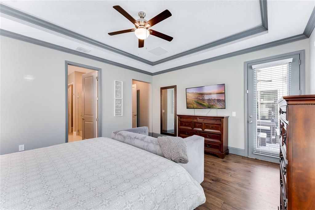 The other view of the primary suite bedroom highlighting the trey ceiling with crown molding and a door out to the lanai.