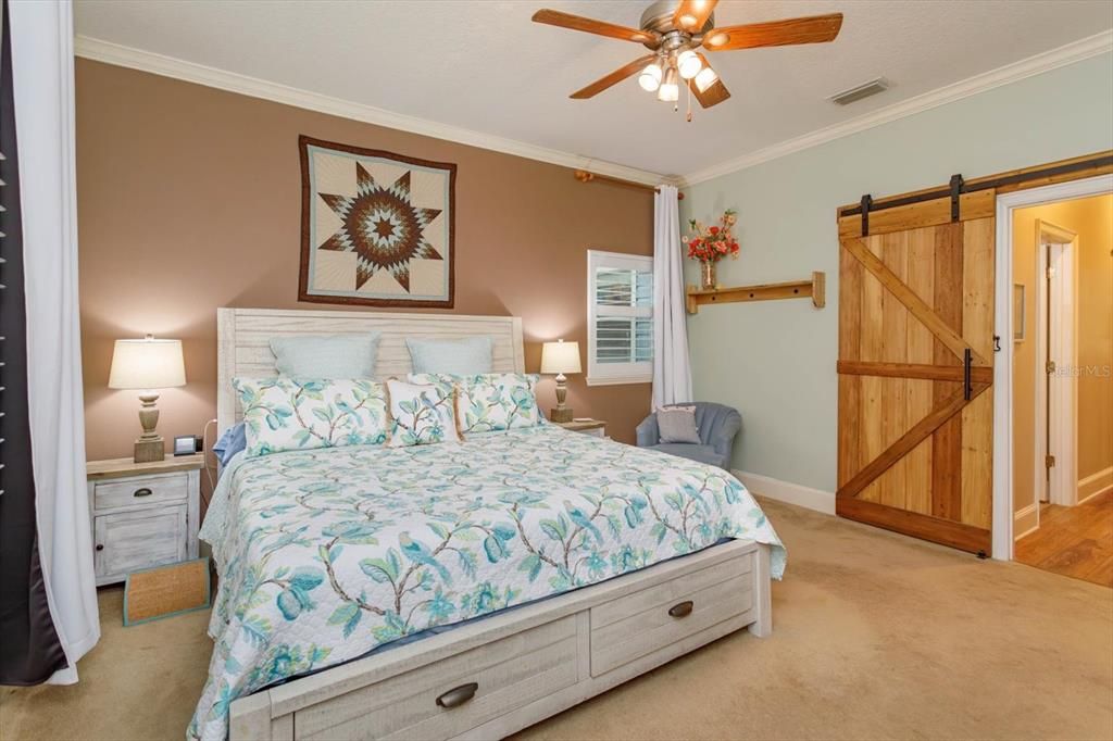 15' x 14' primary bedroom with custom barn door, crown molding and ceiling fan