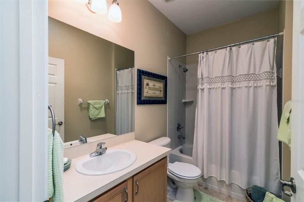 The guest bath has an elevated vanity, upgraded light fixtures, elongated stool, and combination shower and tub with ceramic tile surround.