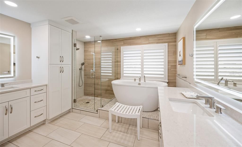 Newly renovated primary bathroom with soaking tub, shower, two vanities and floor to ceiling storage cabinet.