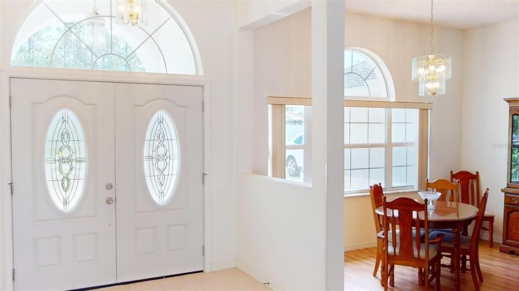 The foyer is welcoming, featuring a double door entryway lit by decorative leaded oval glass, with a large arched transom window above, cascading natural light into the space and creating an elegant, open feel as you step inside. This architectural detail sets a tone of sophistication from the first moment of arrival.
