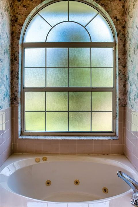 The master bathroom boasts a luxurious jetted tub positioned beneath a large arched window, creating a serene bathing experience as natural light pours in, adding a sense of tranquility and openness to the space. This thoughtful placement enhances relaxation, making the tub not just a bath but a retreat within the home.