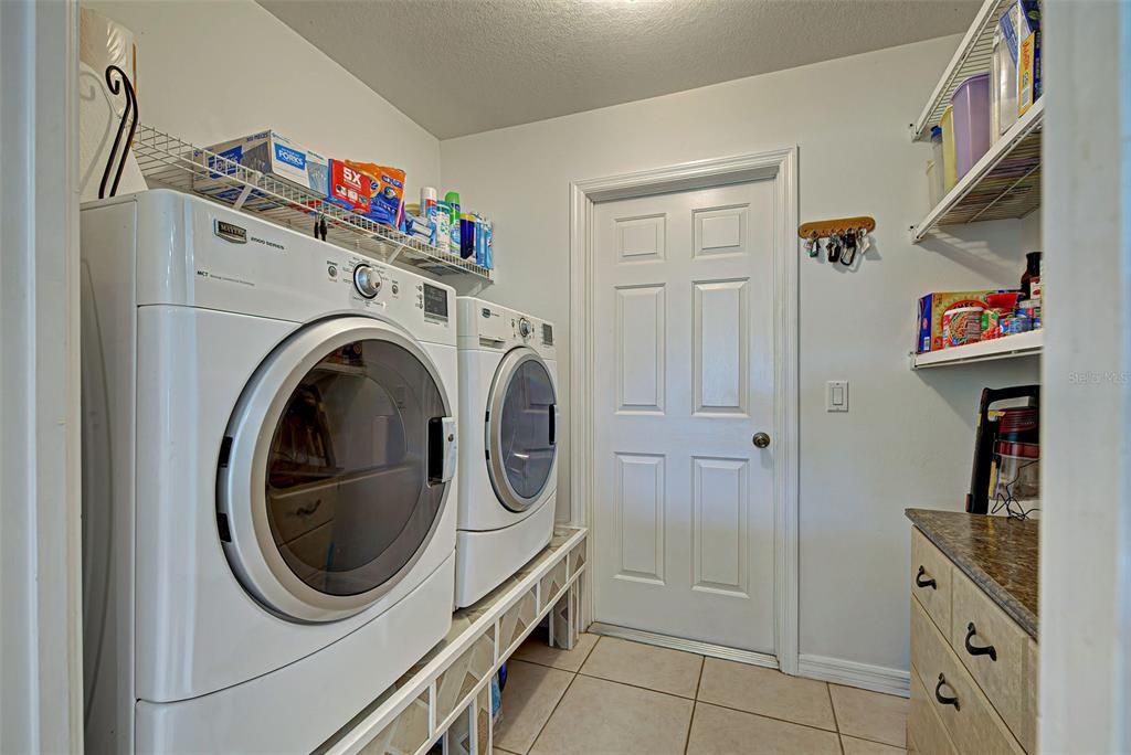 Large laundry room includes room for storage above the cabinet as well as on the shef above the washer and dryer and underneath them.