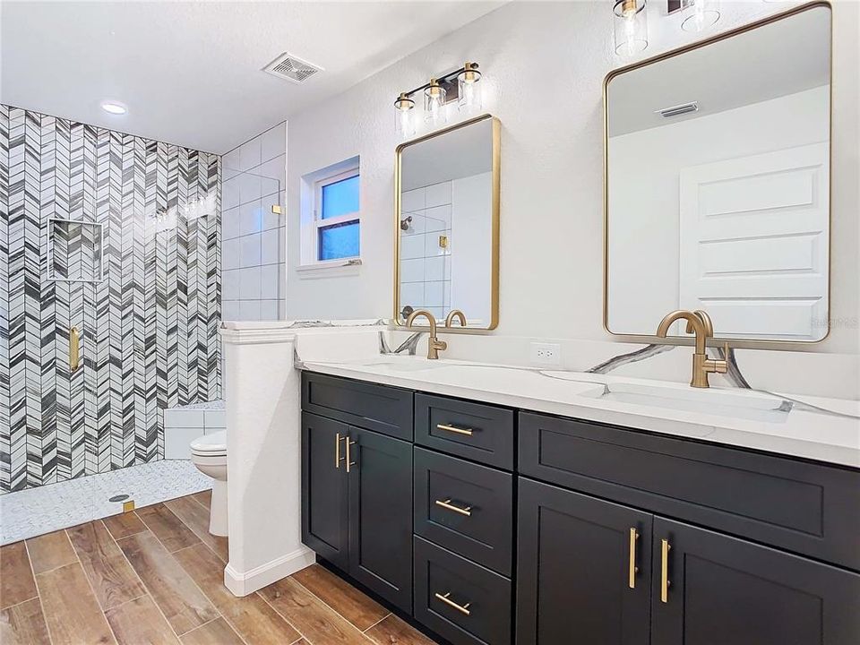 Primary bathroom with double vanity, quartz counters and gold fixtures.