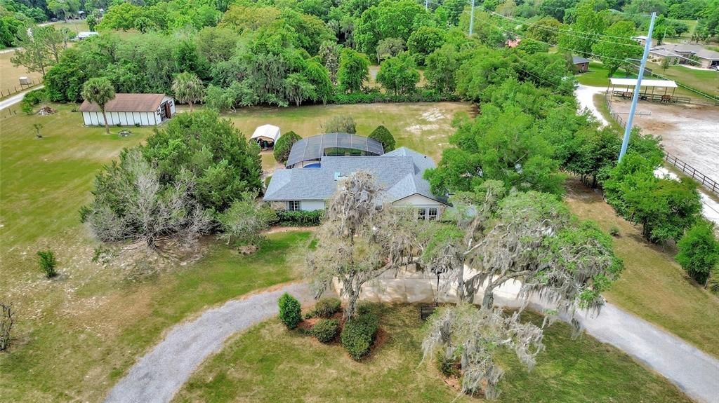 Aerial photo showing home, circular driveway, screened pool enclosure, car port (covering well pump and water treatment system), and barn.
