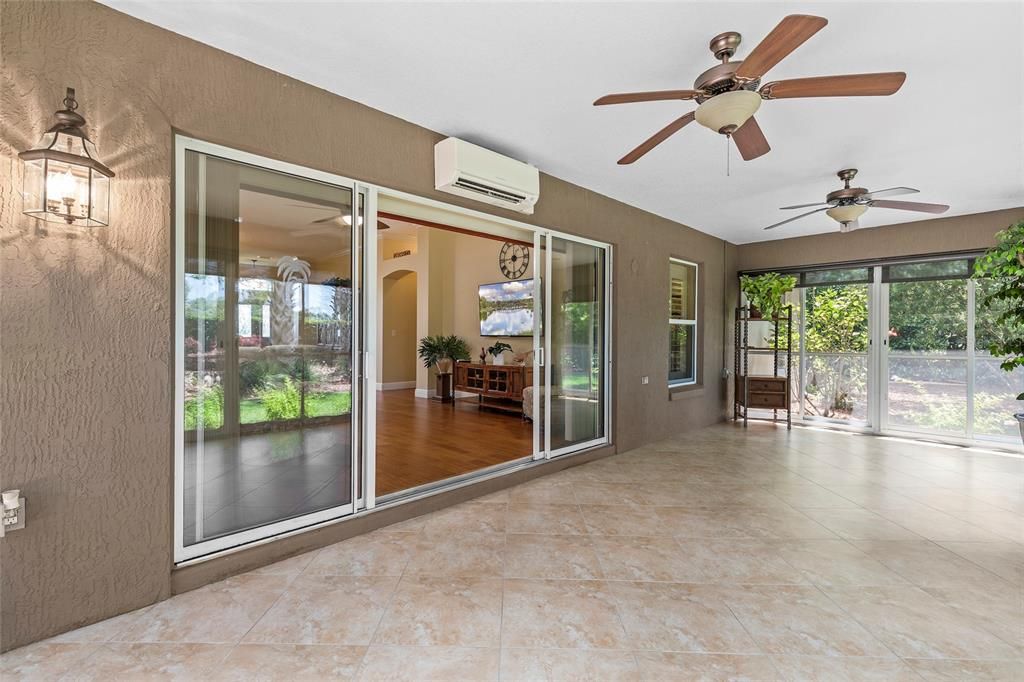 Enclosed lanai off living room with mini-split unit, ceiling fans, sliding doors with screens, pull-down sunshades, tiled floors on diagonal.