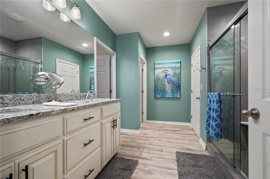 Master Bathroom with tall vanities, two sinks, granite counters, LVP floors, tile shower with glass doors, walk-in closet with laundry room, 2 additional closets and WC