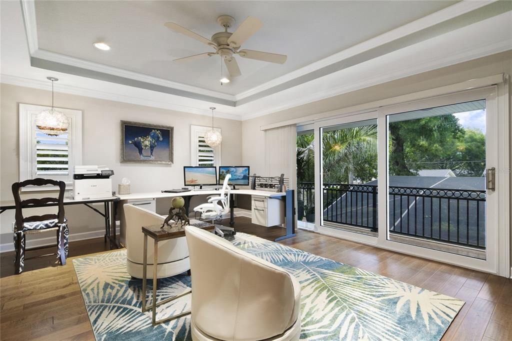 Presently, the seller is using the second-floor primary bedroom as a home office. It has wood floors, a balcony overlooking the pool, and a trey ceiling with a three-piece slider.