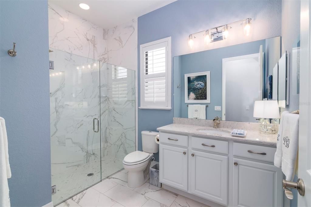the guest bath has a glass enclosed stall shower, elongated stool, elevated vanity with stone counter, upgraded lighting and plumbing fixtures.