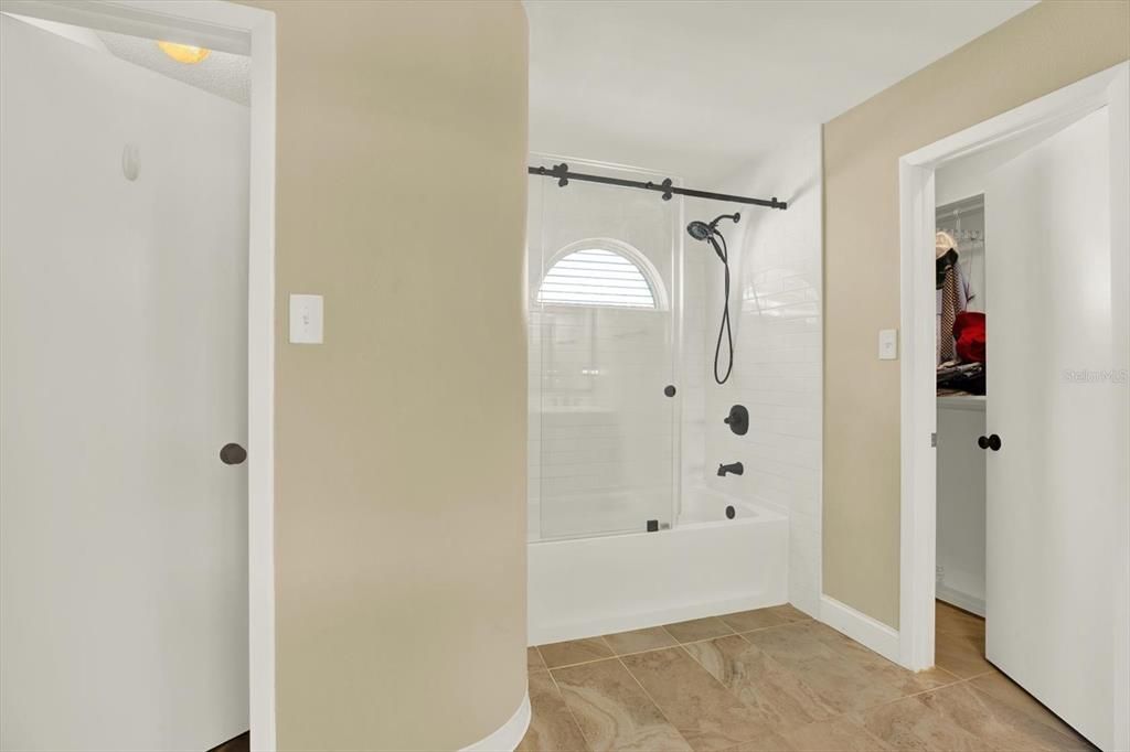 Primary bathroom with two walk in closets and tub/shower combo with glass doors