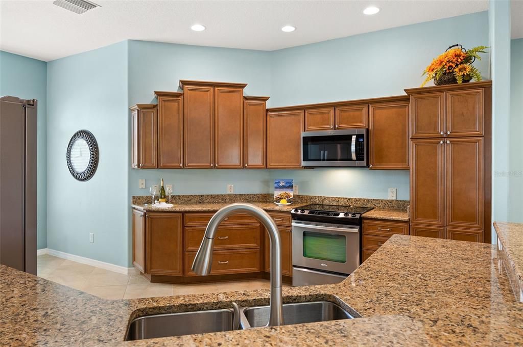 The spacious kitchen boasts granite countertops, light cherry stair step cabinetry with top crown trim, pull-outs, stainless steel appliances, and a generous double door pantry.
