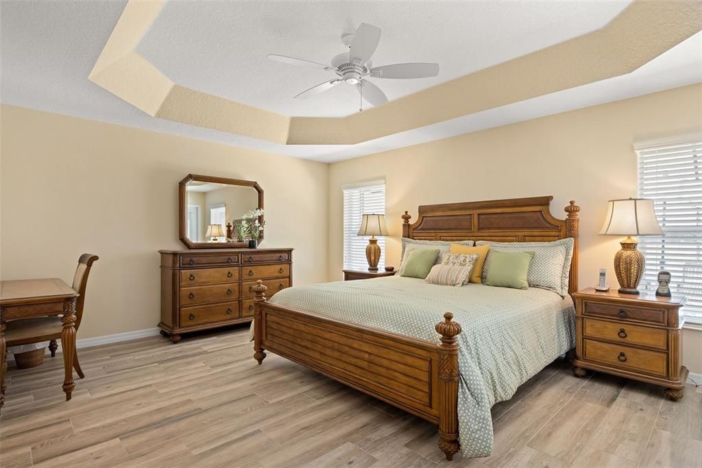 The primary bedroom boasts tray ceilings, views of the golf course, and wood look tile.
