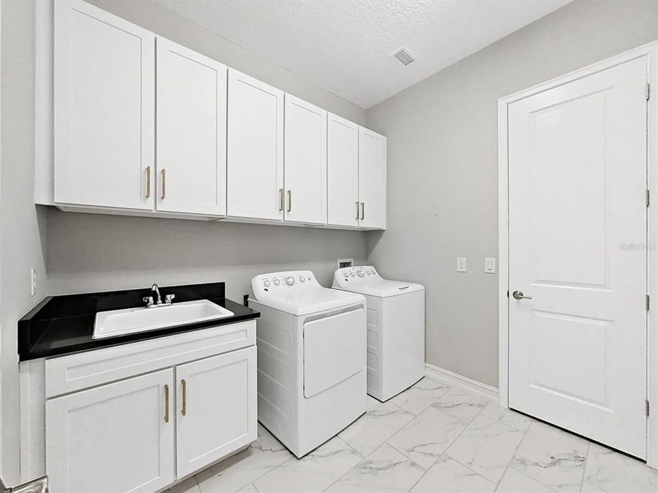 Laundry room features laundry sink, upper cabinets and 2 generous storage closets