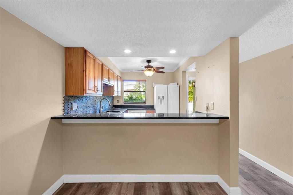 space for some barstools at the eat-in counter looking from living room into the kitchen; hallway to the right leads to the front door, and the stairs that go up; the downstairs 1/2 bath is just out of frame to the right