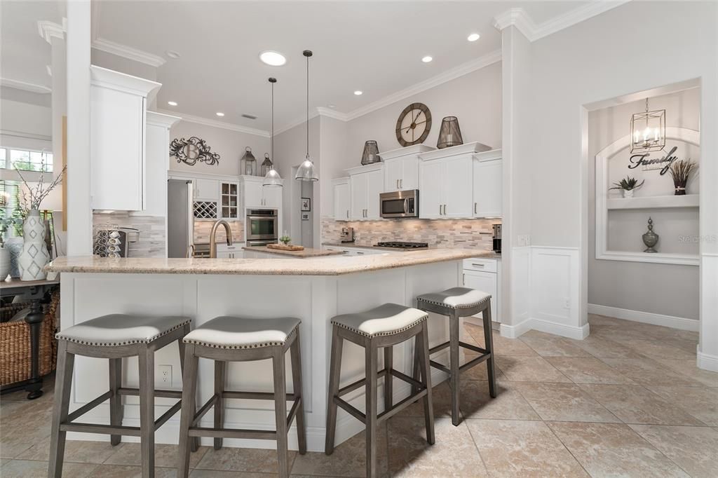 Gorgeous KITCHEN with 2 SOLAR TUBES, STAIR STEPPED upper cabinets w/ CROWN MOLDING & underlighting, new gold hardware for cabinets, new gold plumbing fixtures, GRANITE COUNTERTOPS, chic TILE BACKSPLASH, PENDANT LIGHTING over island, UPGRADED SS APPLIANCES, & pony BREAKFAST BAR.
