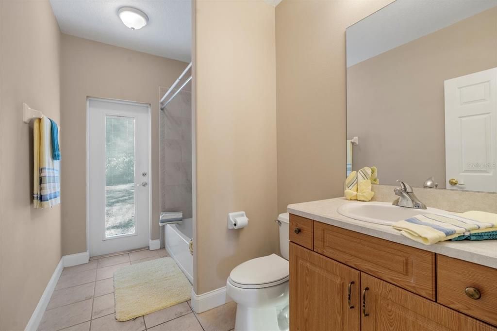 Second bath, single vanity with extended counter, tub with tile shower, pool bath door