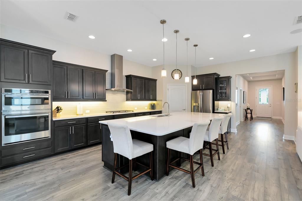 The gourmet kitchen is a chef's delight, boasting 42’ cabinets, under-cabinet lighting, pull-out drawers, upgraded quartz countertops and island, stainless steel appliances, and a stylish tile backsplash.