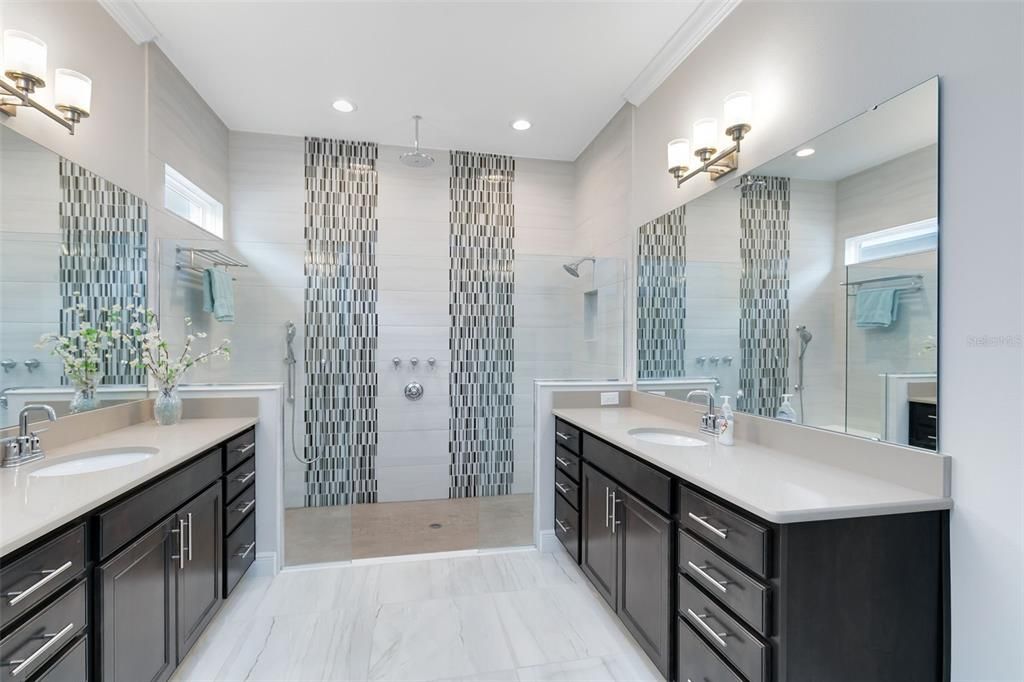 The ensuite master bath is a true retreat, showcasing separate vanities and a spectacular zero entry shower with three shower heads and stunning accent tilework.