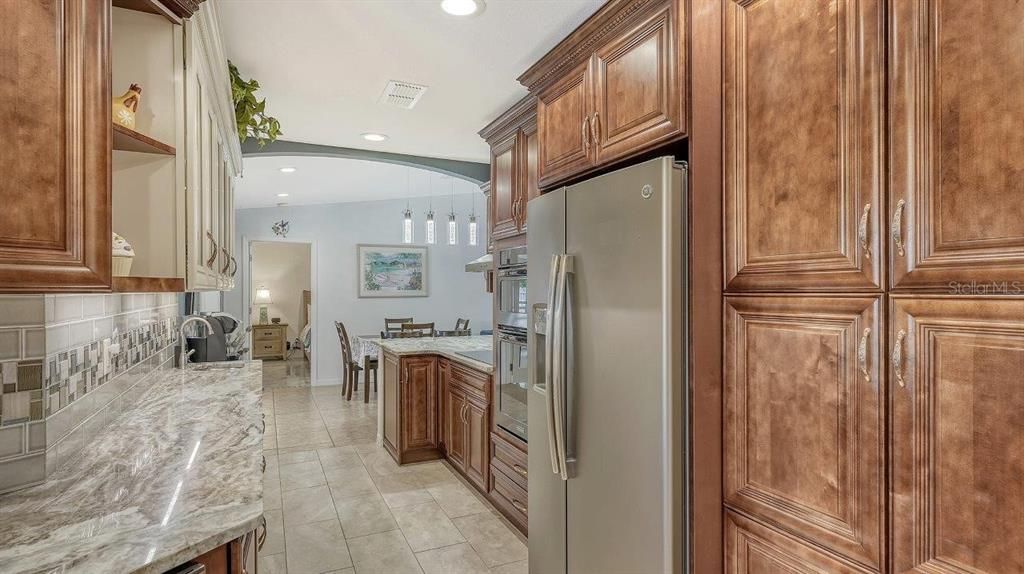 Galley style kitchen featuring granite countertops, a breakfast bar, wet bar, wood cabinetry, and stainless steel appliances.