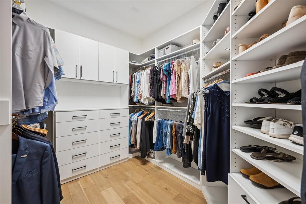 Primary walk in closet with custom shelving & cabinets