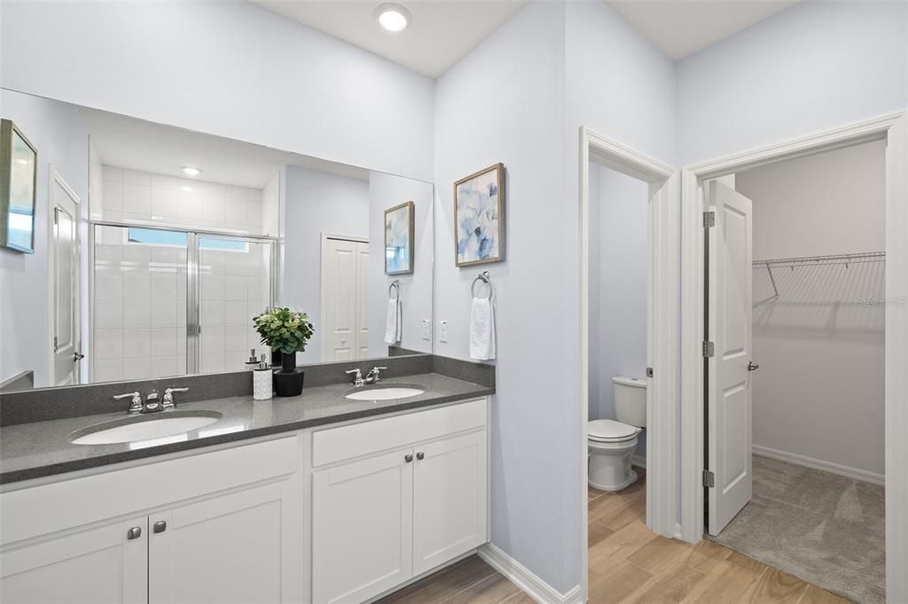 Primary bathroom with a walk-in shower, double vanity sinks, quartz countertops, private toilet closet and a large walk-in closet.