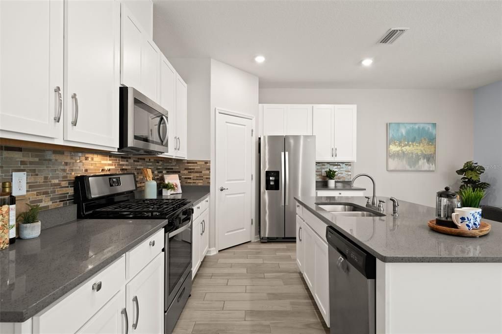 Upgraded kitchen featuring quartz countertops, walk-in pantry, gas stove, stainless steel appliances, cabinet pulls, neutral backsplash and a large island.