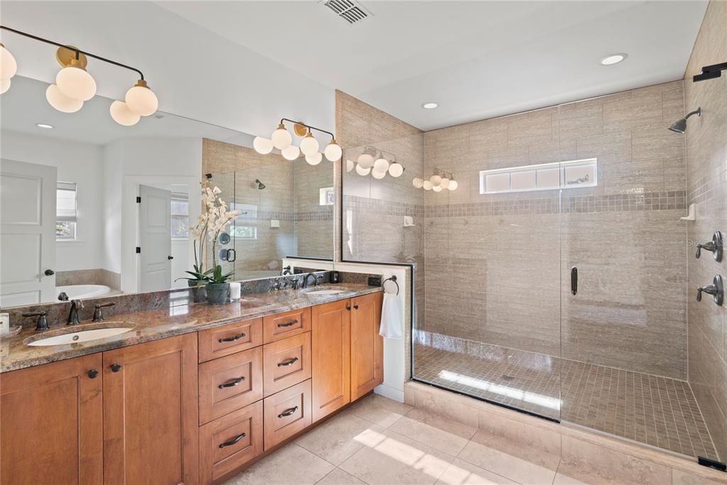 Spacious primary bathroom with dual sinks, large glass-enclosed shower, toilet closet and soak tub