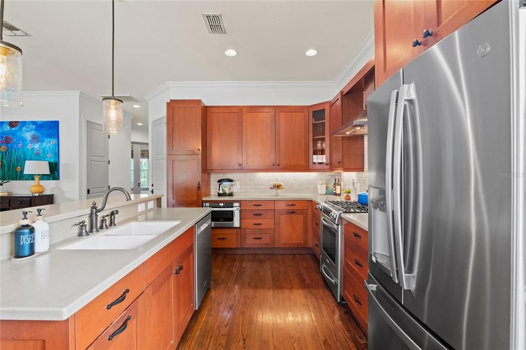 Kitchen with beautiful wood cabinetry, stainless steel appliances, bar seating with pendant lights, gas range and range hood