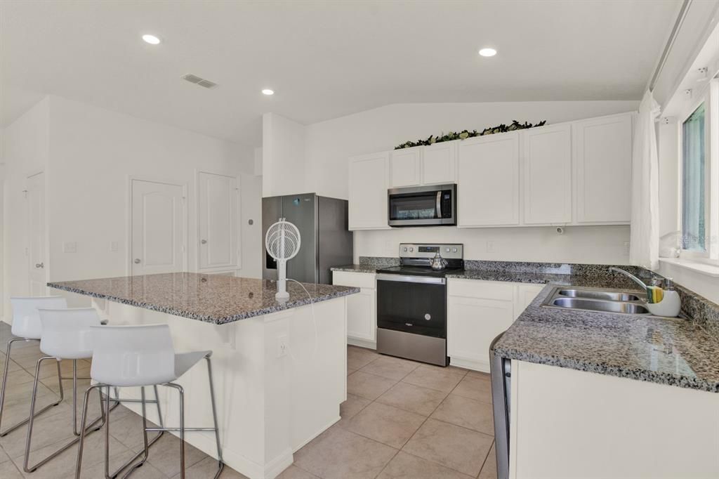 Kitchen with large granite island, white cabinets and large tile flooring