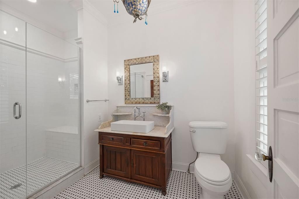 Luxurious primary bathroom including custom vanity with marble top, gorgeous bridge faucet and vintage lighting