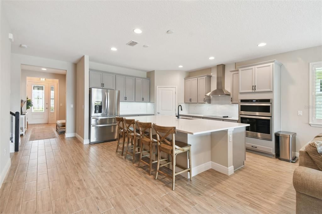 The kitchen is a chef's dream, featuring quartz countertops, 42-inch cabinets, stainless steel appliances, a built-in microwave and oven, cooktop, and a large island with seating, overlooking the dining room and family room.