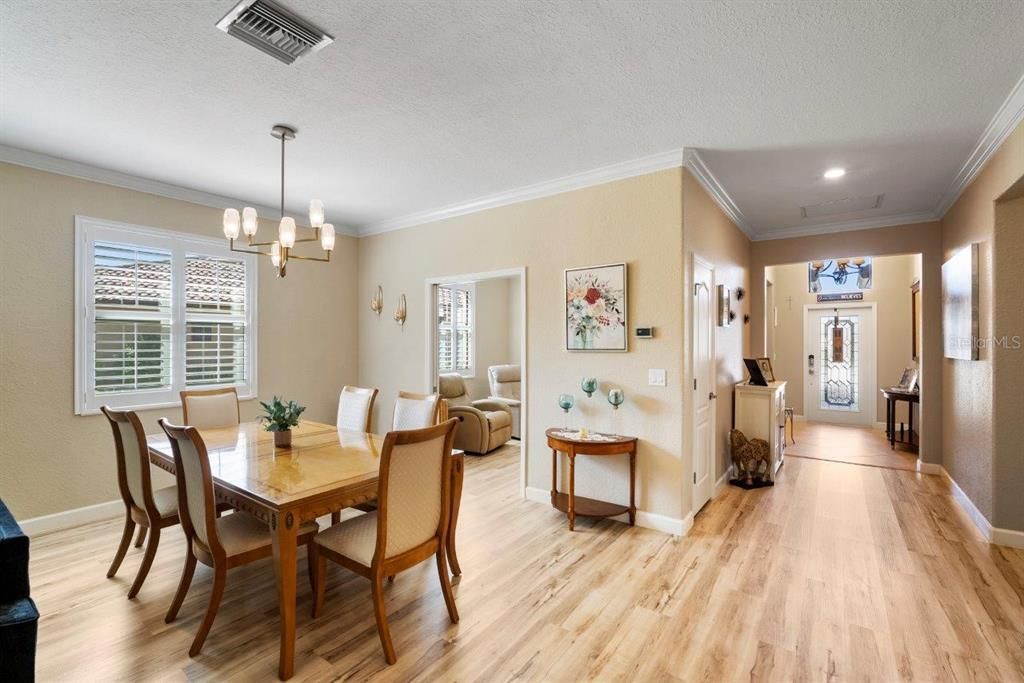 Large great room featuring laminate flooring, plantation shutters, crown molding, and a neutral color pallet.